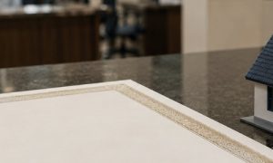 Certidão sobre a mesa ao lado de uma maquete de casa em um ambiente de cartório, representando processos ligados a imóveis e documentação oficial.