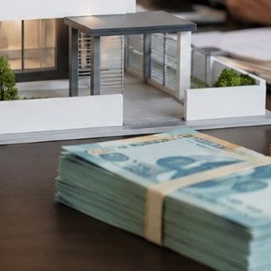 Maquete de imóvel sobre uma mesa de cartório ao lado de maços de dinheiro em reais, em um ambiente institucional elegante e realista, com iluminação suave e enquadramento profissional.