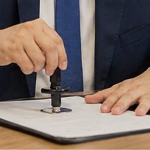 Funcionário de cartório carimbando um documento em uma mesa de atendimento, em ambiente profissional, organizado e com iluminação natural